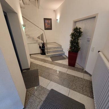 Treppenhaus mit Marmorboden, Pflanze, und Kunstwerk an der Wand.