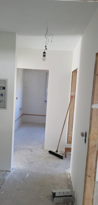 Flur mit weißen Wänden, unmöbliert, Boden vorbereitend, Lichtquelle oben.