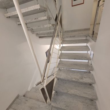 Treppenhaus mit grauen Stufen und einem Geländer, heller Wandanstrich.
