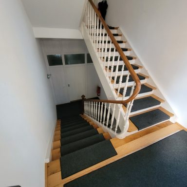 Gerade Treppe mit Holzgeländer, Teppichstufen und hellem, neutralem Wanddesign.